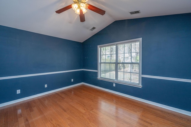 empty room featuring vaulted ceiling, visible vents, baseboards, and wood finished floors