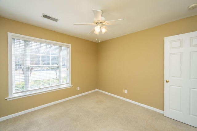 empty room featuring a ceiling fan, light colored carpet, visible vents, and baseboards