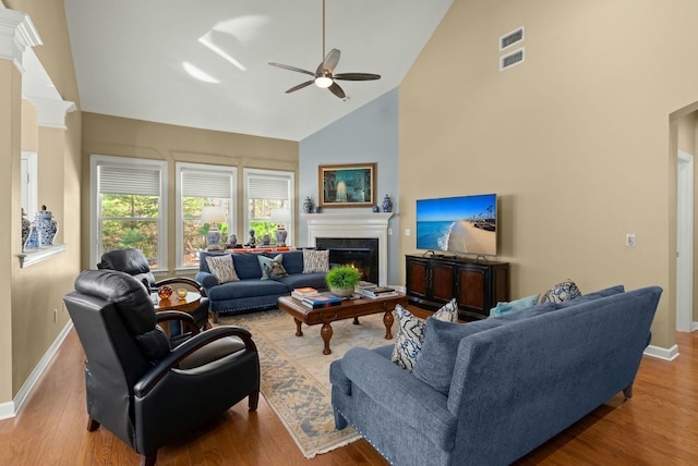 living area with a lit fireplace, high vaulted ceiling, wood finished floors, and baseboards