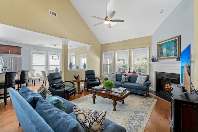 living room featuring a fireplace, decorative columns, visible vents, high vaulted ceiling, and light wood-type flooring