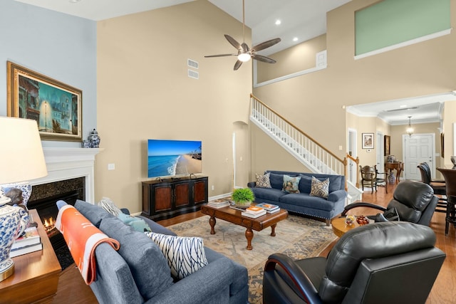 living area with wood finished floors, a lit fireplace, stairs, a high ceiling, and recessed lighting