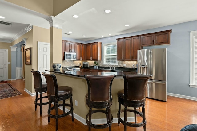 kitchen with visible vents, a kitchen breakfast bar, appliances with stainless steel finishes, light wood finished floors, and decorative columns