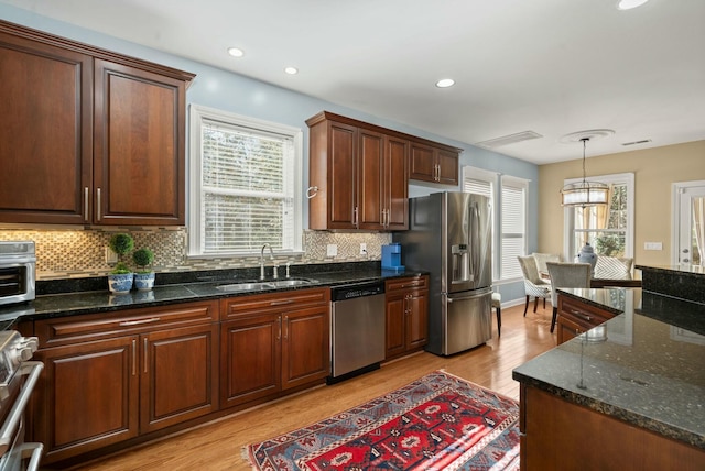 kitchen featuring tasteful backsplash, light wood-style flooring, appliances with stainless steel finishes, pendant lighting, and a sink