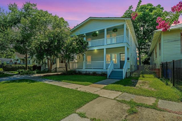 view of front of home featuring a front yard, covered porch, fence, a balcony, and a gate