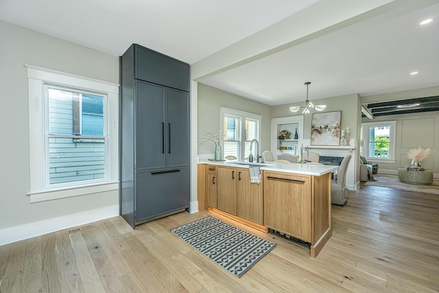 kitchen with light wood-type flooring, a chandelier, a peninsula, light countertops, and a sink