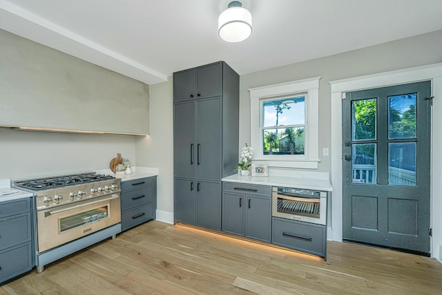 kitchen featuring gray cabinets, light countertops, light wood finished floors, and high end range