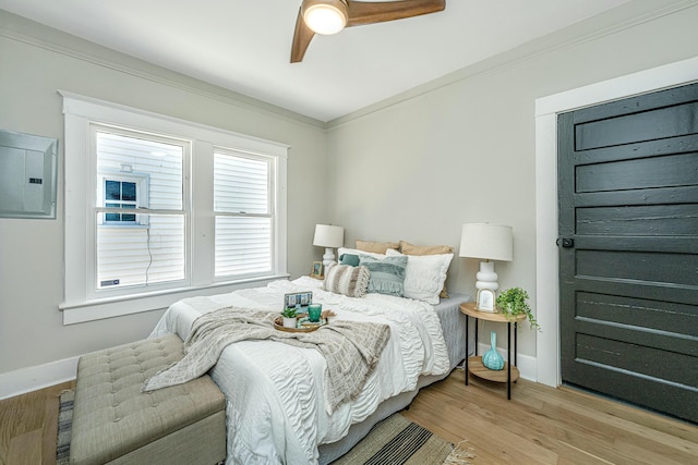 bedroom with electric panel, light wood-style flooring, baseboards, and crown molding
