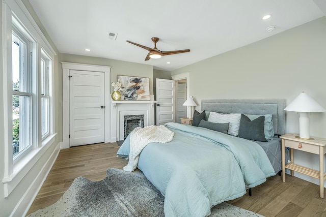 bedroom featuring recessed lighting, a fireplace, a ceiling fan, visible vents, and wood finished floors