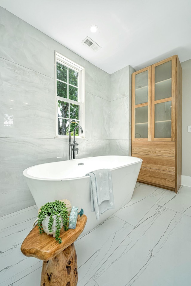 bathroom featuring visible vents, marble finish floor, tile walls, and a soaking tub