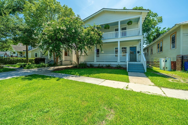 view of front of property featuring a porch, a balcony, fence, and a front lawn