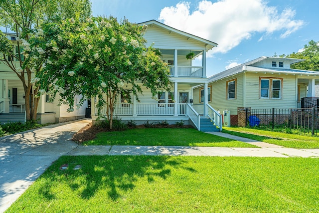 view of front of home with covered porch, fence, a balcony, a front lawn, and driveway