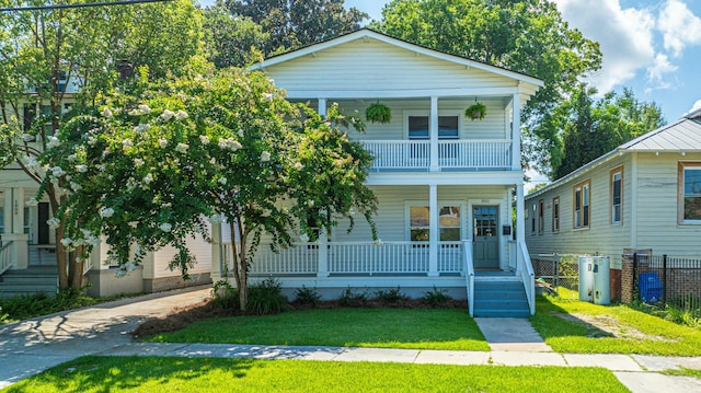 view of front of property with covered porch, fence, a front lawn, and a balcony
