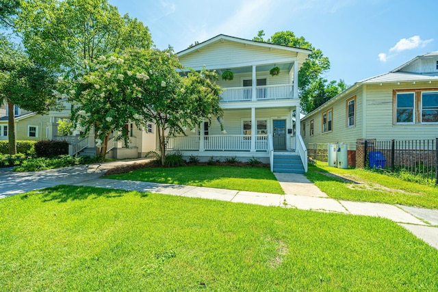 view of front of home with a front yard, a porch, fence, and a balcony