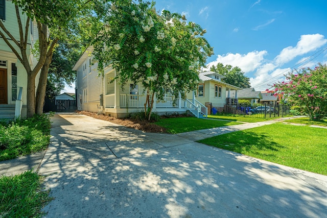 view of front facade with a front yard, fence, covered porch, and concrete driveway