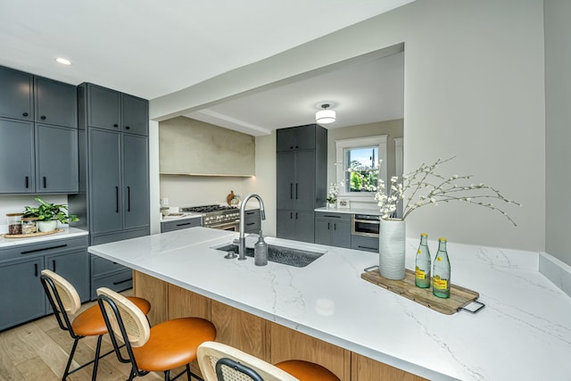 kitchen with light wood-type flooring, light stone counters, a peninsula, a breakfast bar area, and a sink