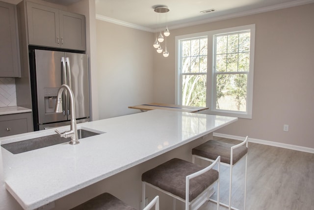 kitchen featuring light wood finished floors, tasteful backsplash, gray cabinetry, ornamental molding, and stainless steel fridge