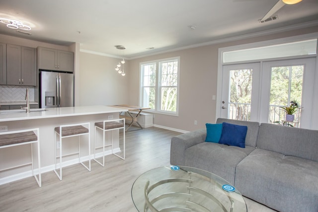 living area featuring baseboards, ornamental molding, visible vents, and light wood-style floors