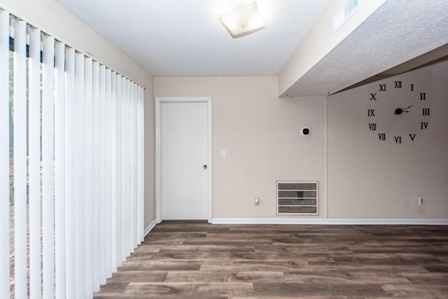 empty room with a textured ceiling, heating unit, and dark wood-type flooring