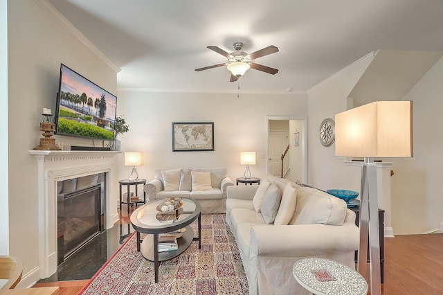 living area featuring wood finished floors, a fireplace with flush hearth, ornamental molding, and a ceiling fan