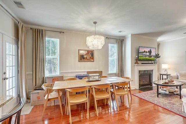 dining room featuring visible vents, a fireplace with flush hearth, ornamental molding, and light wood finished floors