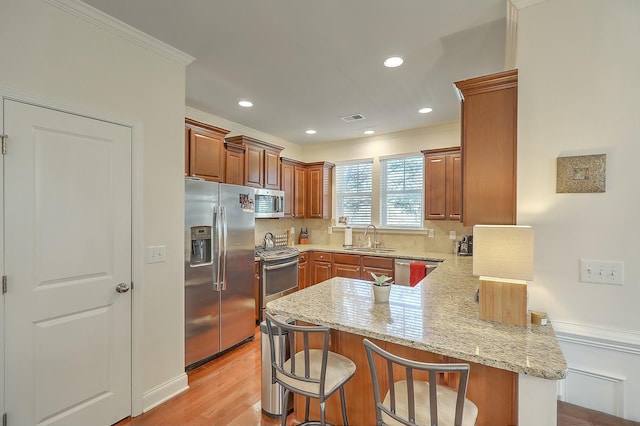 kitchen featuring a breakfast bar area, a peninsula, a sink, decorative backsplash, and stainless steel appliances