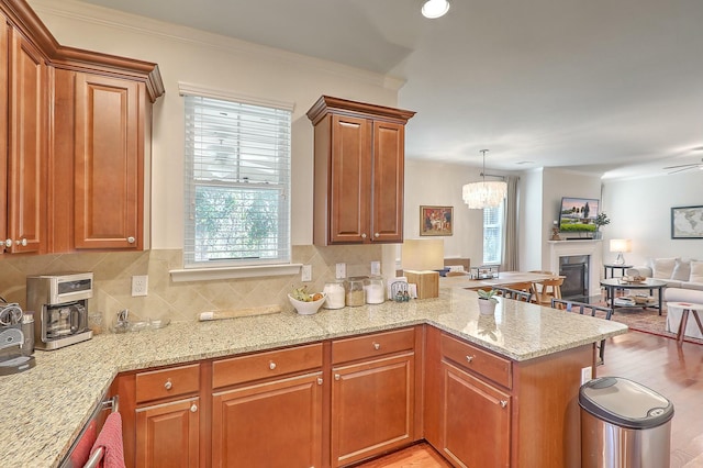 kitchen featuring backsplash, crown molding, open floor plan, light stone counters, and a peninsula