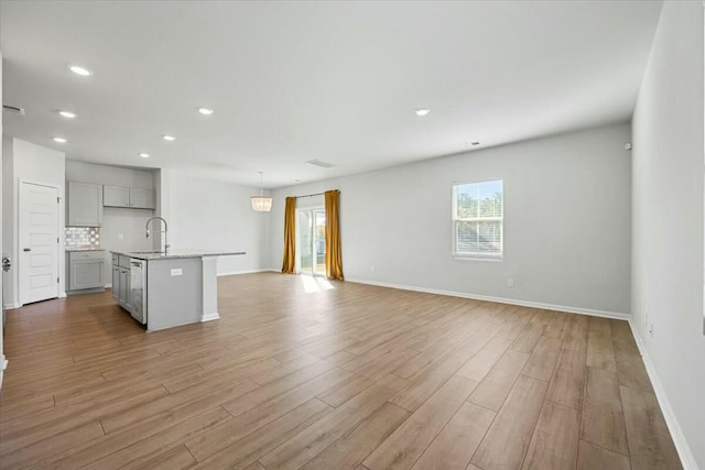 kitchen featuring backsplash, gray cabinetry, a kitchen island with sink, and light hardwood / wood-style floors