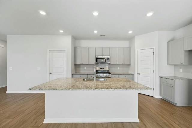 kitchen featuring a kitchen island with sink, stainless steel appliances, light stone counters, and light wood-type flooring