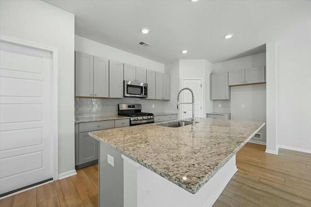 kitchen featuring stainless steel appliances, gray cabinets, a kitchen island with sink, and sink