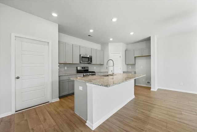 kitchen featuring appliances with stainless steel finishes, an island with sink, gray cabinetry, and sink