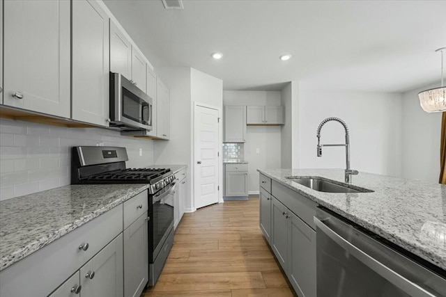 kitchen with light stone countertops, appliances with stainless steel finishes, light wood-type flooring, and pendant lighting