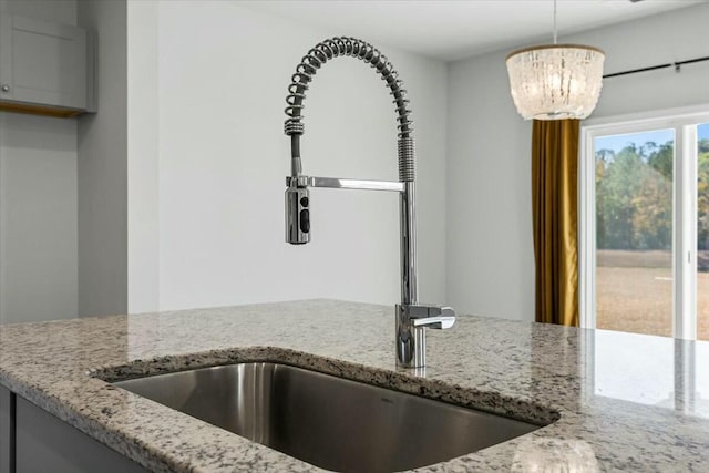 kitchen with light stone counters, sink, hanging light fixtures, and a notable chandelier