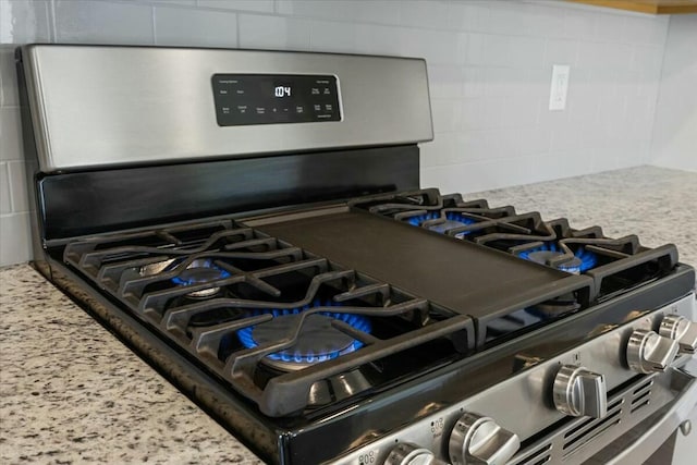 details featuring decorative backsplash, light stone counters, and stainless steel gas range