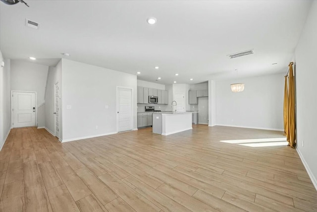 unfurnished living room with a notable chandelier, sink, and light hardwood / wood-style flooring