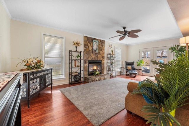 living room featuring a stone fireplace, wood finished floors, a ceiling fan, french doors, and crown molding