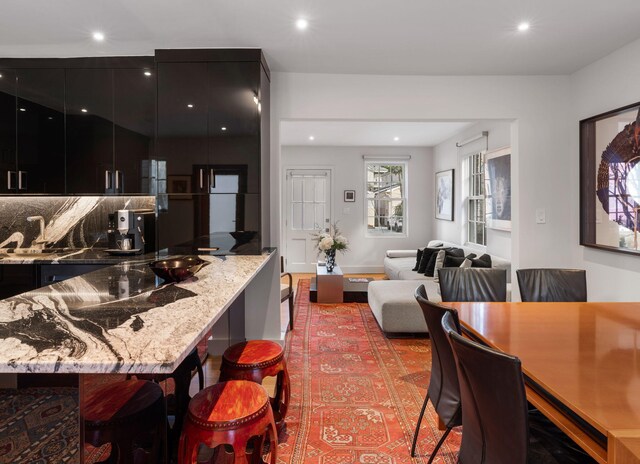 301 Broad St Unit 1, Charleston, SC 29401 - kitchen with dark cabinets, a kitchen bar, light stone countertops, modern cabinets, and recessed lighting