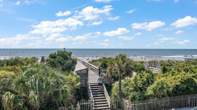 property view of water featuring stairway, fence, and a view of the beach