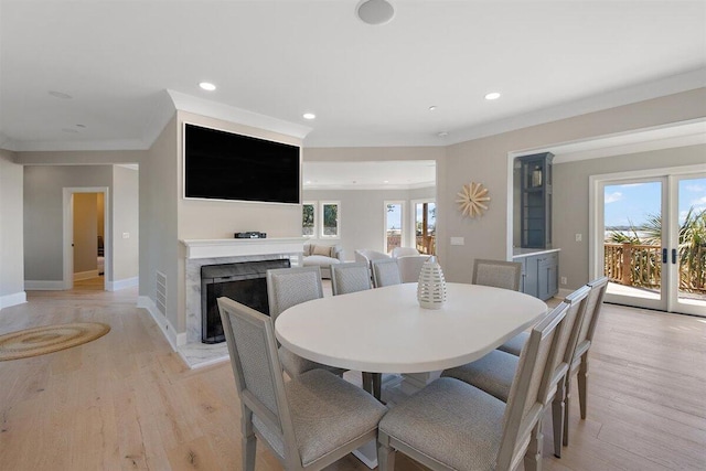 dining area featuring a premium fireplace, ornamental molding, and light wood-type flooring