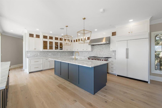 kitchen featuring sink, paneled built in refrigerator, a kitchen island with sink, white cabinets, and decorative light fixtures