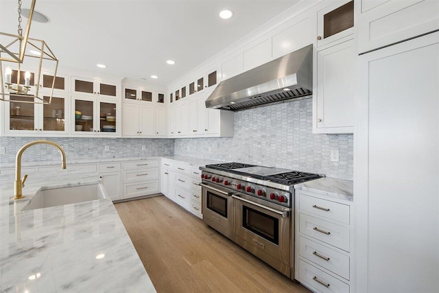 kitchen featuring wall chimney exhaust hood, sink, double oven range, pendant lighting, and white cabinets