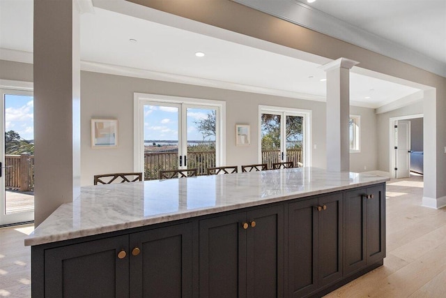 kitchen featuring a breakfast bar area, decorative columns, light stone counters, a wealth of natural light, and ornamental molding