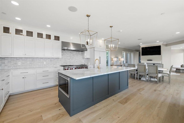 kitchen with a center island with sink, stainless steel microwave, white cabinets, and decorative light fixtures