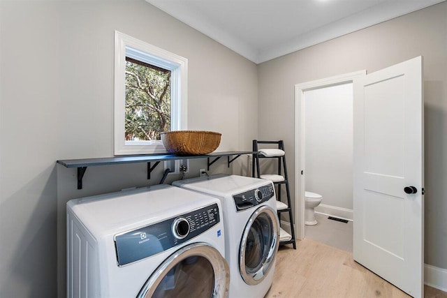 laundry area featuring crown molding, washer and clothes dryer, and light hardwood / wood-style floors