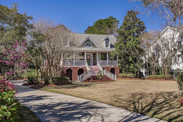 beach home featuring brick siding, stairway, a porch, and a front yard