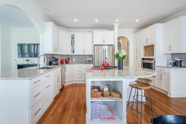 kitchen with a kitchen bar, open shelves, appliances with stainless steel finishes, and a sink