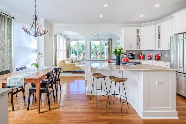 kitchen with tasteful backsplash, crown molding, light wood-type flooring, high end refrigerator, and white cabinets