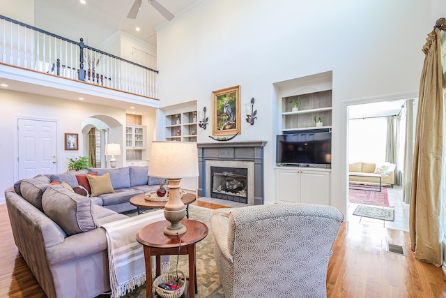 living room with visible vents, built in shelves, a fireplace with flush hearth, wood finished floors, and arched walkways