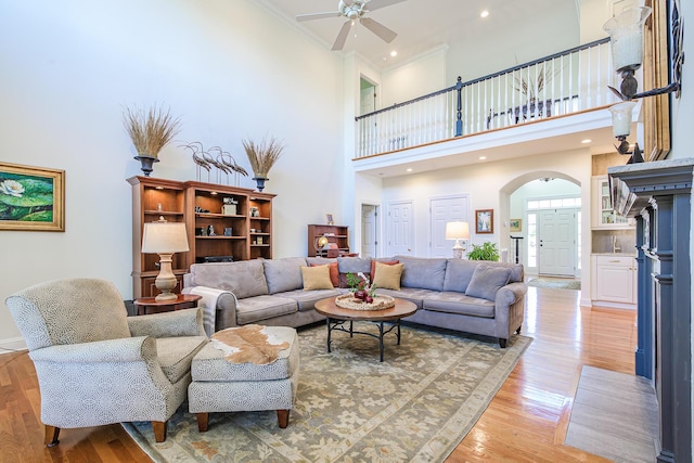 living room with light wood finished floors, ceiling fan, ornamental molding, a towering ceiling, and arched walkways