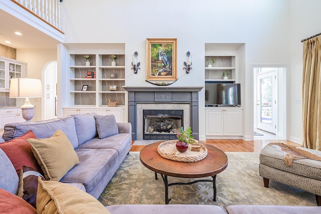 living room with built in shelves, a high ceiling, a fireplace, arched walkways, and light wood-type flooring