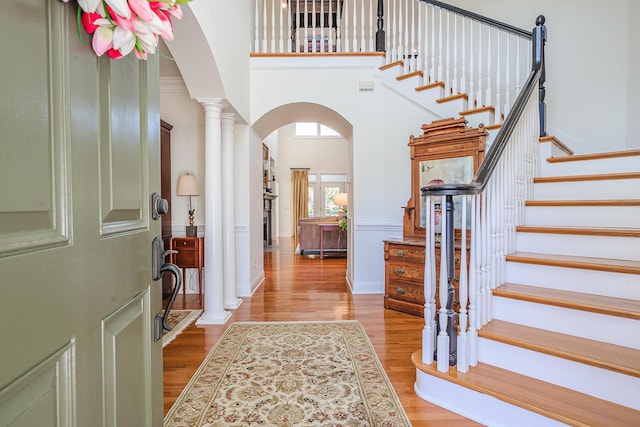 entrance foyer featuring wood finished floors, arched walkways, a towering ceiling, stairs, and ornate columns